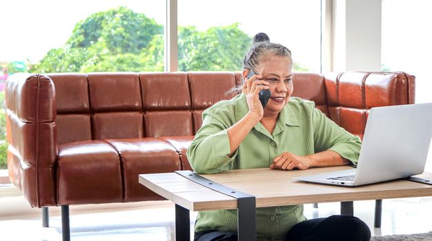 Asian women Retirement Use a smartphone and laptop in the living room concept to work at home. Quarantine to prevent spreading disease Or a conversation with someone far away Via the Internet