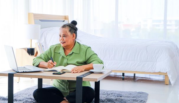 Senior woman retiring Asian Work, write and use the computer at the desk in the relaxing room. And working at the home of retirement