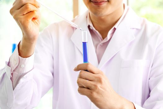 An Asian scientist or chemist drops a blue liquid chemical in a laboratory. Research concepts in healthcare, pharmacy, and medicine. Liquid analysis to separate DNA and molecules in vitro.