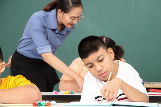 Asian disabled children Or, an autistic child learns to read, write, and train their hand and finger muscles with a teacher at their classroom desk. Concentrate and smile Happy disability kid concept