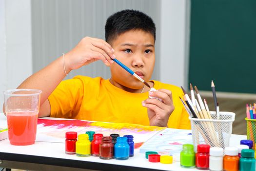 A handicapped Asian girl is practicing hand and finger muscles by drawing and painting with water. With a helping teacher to care for happiness and concentration in the classroom