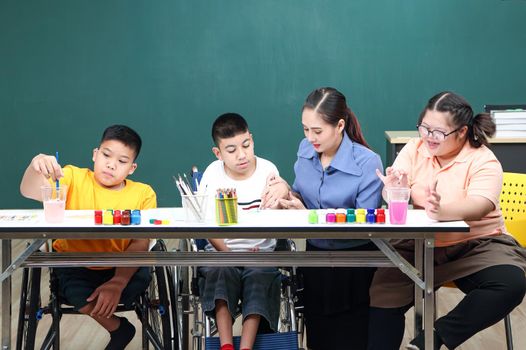 A handicapped Asian girl is practicing hand and finger muscles by drawing and painting with water. With a helping teacher to care for happiness and concentration in the classroom