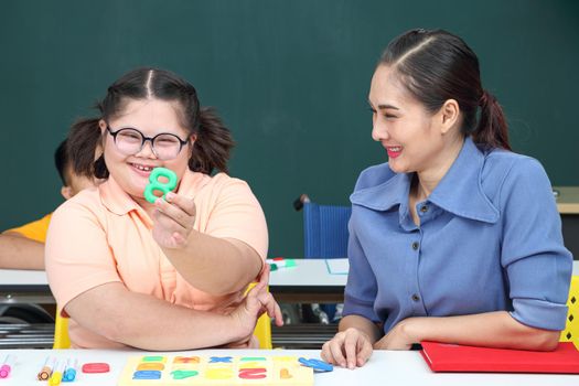 Asian disabled children Or, an autistic child learns to read, write, and train their hand and finger muscles with a teacher at their classroom desk. Concentrate and smile Happy disability kid concept