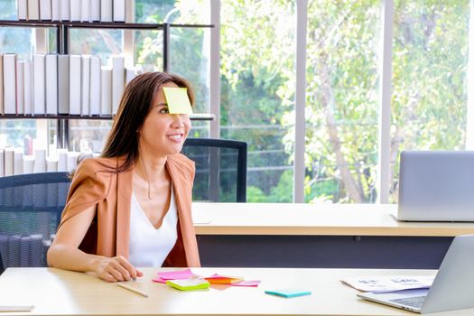 Asian businesswomen look and write a post-it note on their faces to relax and smile from work. Work plan, brainstorm, strategy Creative Lifestyle, Success in Business Concept