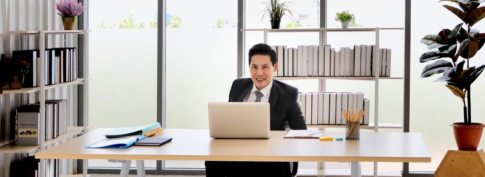 Portrait of a cheerful Asian business man sitting at a desk looking at the PC screen, fists make him look good, read amazing news, celebrate the success.