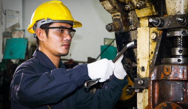 Asian male worker In industries that wear glasses, safety hats and safety uniforms Wrench tool holder stand Machine maintenance technician operation concept In an industrial factory with confidence