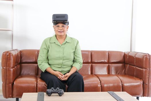 Retired Asian women are enjoying VR  glasses for advanced augmented reality headsets in an amazing 3D format on the couch, the concept of technological innovation, and relaxing fun. For adults at home