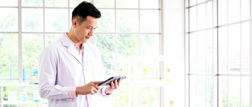 An Asian scientist or researcher wearing white clothes. He carried a tablet with a science lab and Laboratory test tubes during working hours In the concept of corona vaccine research and development