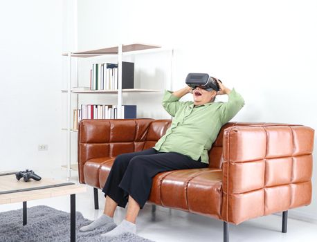 Retired Asian women are enjoying VR  glasses for advanced augmented reality headsets in an amazing 3D format on the couch, the concept of technological innovation, and relaxing fun. For adults at home