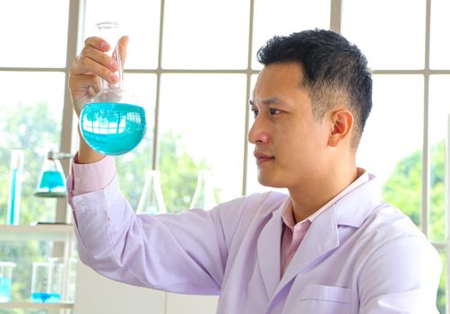 Asian scientist or chemist looks at a blue liquid chemical test tube in the laboratory. Research concepts in healthcare, pharmacy, and medicine. Liquid analysis to separate DNA and molecules in vitro.