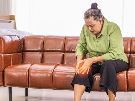 Asian elderly woman Holding the knee in pain while sitting on the sofa in the room Health care concept Women suffering from knee pain, health problems Senior woman and the concept of people