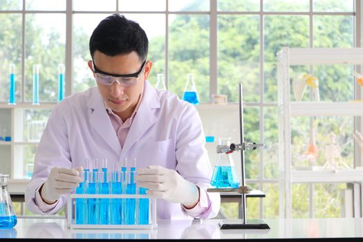 An Asian scientist or chemist drops a blue liquid chemical in a laboratory. Research concepts in healthcare, pharmacy, and medicine. Liquid analysis to separate DNA and molecules in vitro.