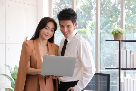 Asian businessmen and women stand and hold laptop looked relaxed, smiling from work. Work plan, brainstorm, strategy Creative Lifestyle, Success in Business Concept