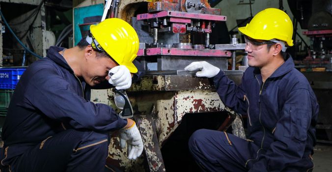 Two skilled Asian workers, dressed in helmet uniforms, were talking to analyze the inspection data. Maintenance of metal printing press The concept of teamwork at the factory