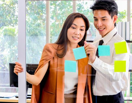 Asian businessmen and women looking and writing post-it notes for brainstorming. Put a post on the mirror in the office Work plan, brainstorm, strategy Creative Lifestyle, Success in Business Concept