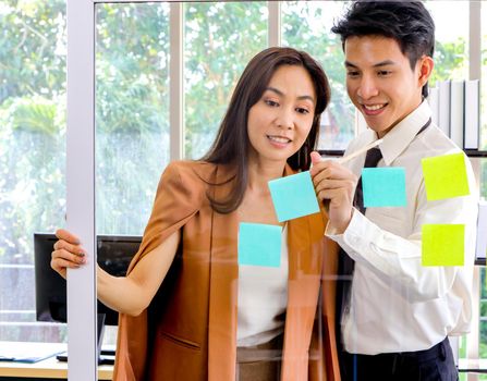 Asian businessmen and women looking and writing post-it notes for brainstorming. Put a post on the mirror in the office Work plan, brainstorm, strategy Creative Lifestyle, Success in Business Concept