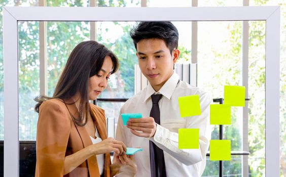 Asian businessmen and women looking and writing post-it notes for brainstorming. Put a post on the mirror in the office Work plan, brainstorm, strategy Creative Lifestyle, Success in Business Concept