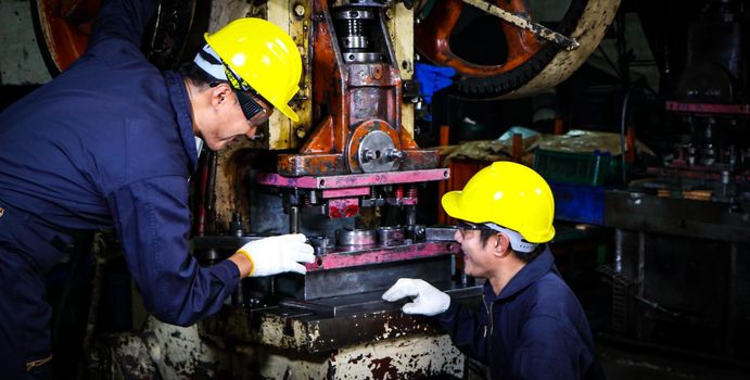 Two skilled Asian workers, dressed in helmet uniforms, were talking to analyze the inspection data. Maintenance of metal printing press The concept of teamwork at the factory