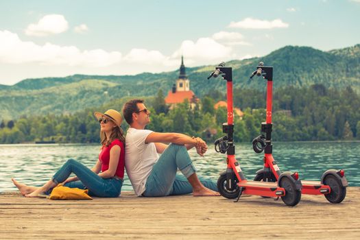 Young couple using electric scooter as modern ecological mean of transport while exploring green country Slovenia at vacations. Green eco energy concept with zero emission. Warm sunshine filter