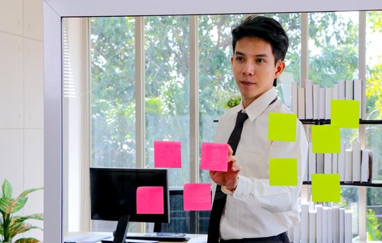 Asian businessmen are looking for and writing post-it notes for brainstorming. Put a post on the mirror in the office Work plan, brainstorm, strategy Creative Lifestyle, Success in Business Concept