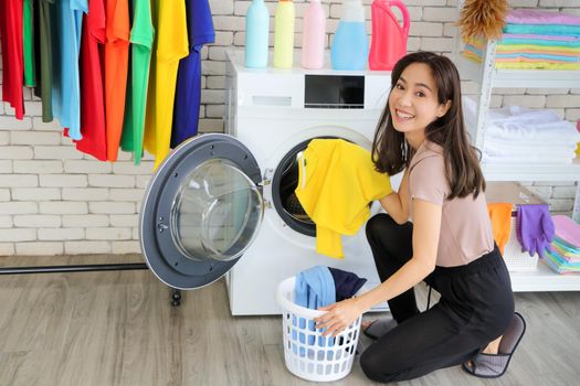 An Asian woman placed a laundry basket beside the washing machine. Pick up clothes from inside the washing machine Looking at the cleanliness and smiling inside the house there are empty floors.