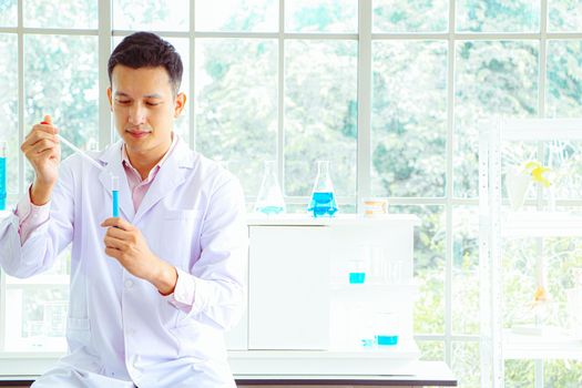 An Asian scientist or chemist drops a blue liquid chemical in a laboratory. Research concepts in healthcare, pharmacy, and medicine. Liquid analysis to separate DNA and molecules in vitro.