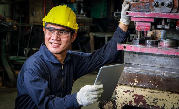 Skilled Asian workers wearing uniform clothing, safety hats, and safety goggles. Are using a tablet to analyze data Metal press maintenance inspection at the factory,concept