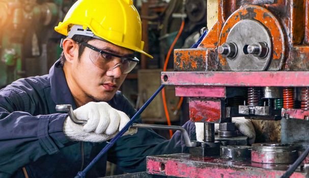 Asian male worker In industries that wear glasses, safety hats and safety uniforms Wrench tool holder stand Machine maintenance technician operation concept In an industrial factory with confidence