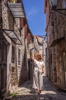 Beautiful blonde young female traveler wearing straw sun hat, taking selfie while sightseeing and enjoying summer vacation in an old traditional costal town at Adriatic cost, Croatia