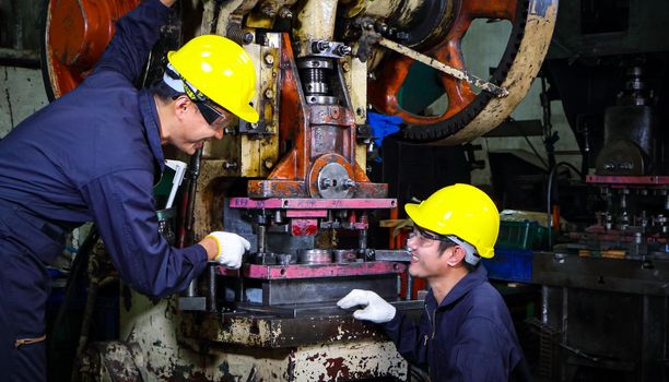 Two skilled Asian workers, dressed in helmet uniforms, were talking to analyze the inspection data. Maintenance of metal printing press The concept of teamwork at the factory