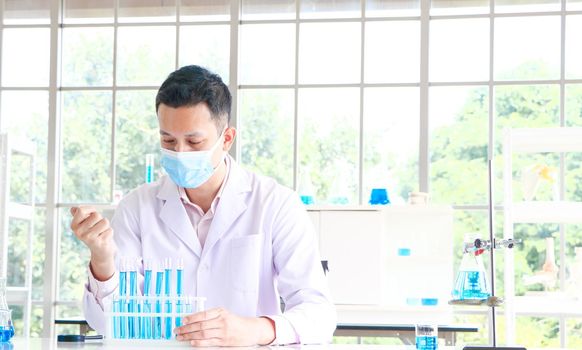 An Asian scientist or chemist drops a blue liquid chemical in a laboratory. Research concepts in healthcare, pharmacy, and medicine. Liquid analysis to separate DNA and molecules in vitro.