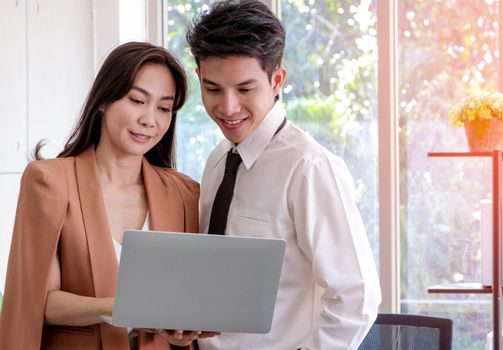 Asian businessmen and women stand and hold laptop looked relaxed, smiling from work. Work plan, brainstorm, strategy Creative Lifestyle, Success in Business Concept