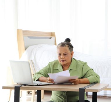 Senior Asian women Carrying documents with a laptop A concept that manages home utility bills or money for older women who use their computers to work or work documents online. Aging and technology