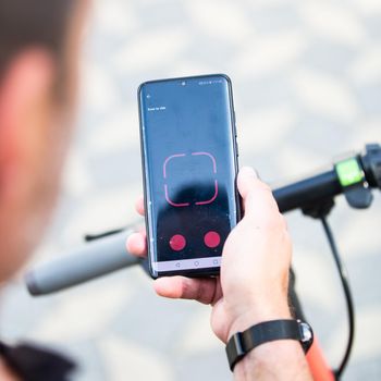 Close up of hand and smartphone, unlocking dockless electric scooter for rent with debranded generic phone app