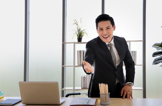 Asian businessman That is positive adults Standing up and standing hands out in a modern office Concepts that work successfully On the computer desk Middle-aged men smile and relax
