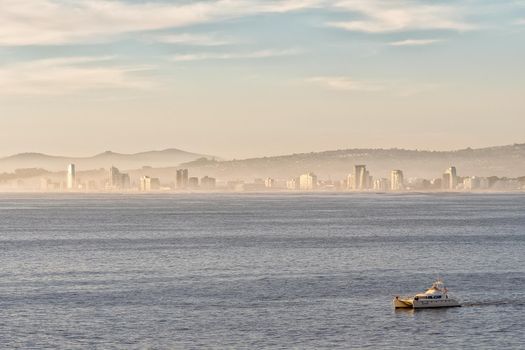 A misty sunset view of Die Strand seen from Clarence Drive accross False Bay. A yacht is visible