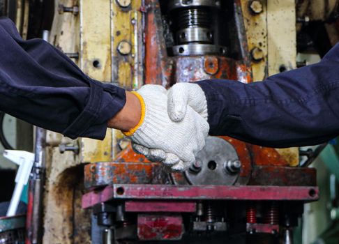 Two skilled Asian workers in uniforms were talking and touching each other with their hands. When the work is done In the maintenance of the metal press, the concept of teamwork at the factory.