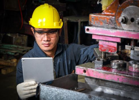 Skilled Asian workers wearing uniform clothing, safety hats, and safety goggles. Are using a tablet to analyze data Metal press maintenance inspection at the factory, concept