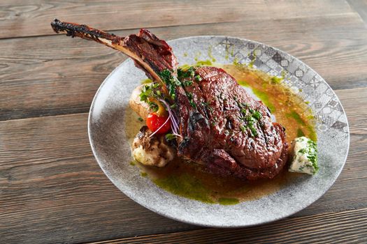 Close up of modern french cuisine. Juicy bbq roasted lamb on bone served with garlic, cheese, vegetables and sauce. Dinner meal isolated on woden table in restaurant. Concept of cuisine, meat.