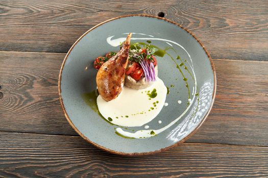 Top view of juicy roasted bbq chicken leg served with mashed potato and mushrooms, fresh green sprouts, cherry tomatoes, sour cream and green sauce. Beautiful blue ceramic plate on wooden table.