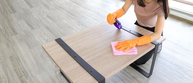 close-up Asian woman The housewife wears protective gloves to do housework, uses products to wipe the table in the living room in the house where the sun is shining. Corona Covid-19 Virus Protection