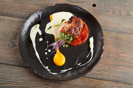 From above view of juicy grilled beef steak served on tomato pillow, egg yolk, white and green sauces and sprouts. Tasty dish presented on wooden table in restaurant. Cuisine concept.