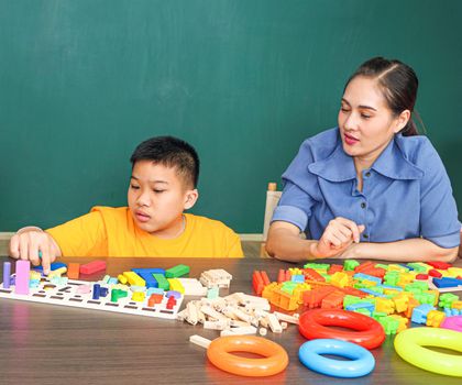 An Asian girl with a disability is practicing the use of hand and finger muscles. By playing with toys With a helping teacher to care for happiness and concentration in the classroom