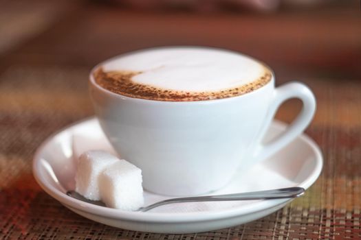 Cup of coffee on a wooden table with two pieces of shugar in cafe