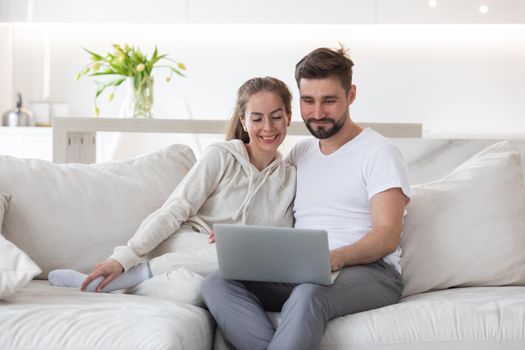 Portrait of mid adult couple relaxing in living room sitting together browsing internet on laptop computer
