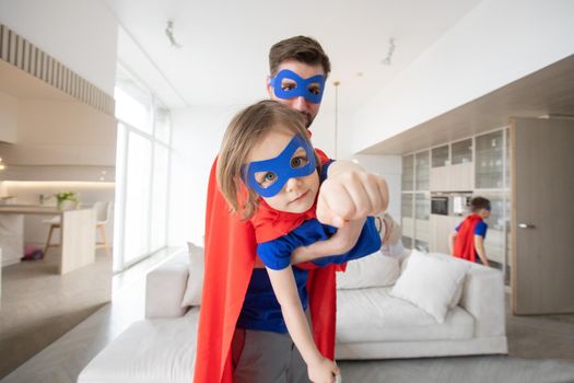 Father holding son flying in superhero costume at home