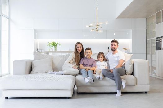 Family portrait of young parents with their two children at home, white modern desgin of living room