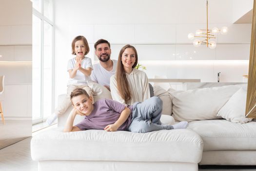 Family portrait of young parents with their two children at home, white modern desgin of living room