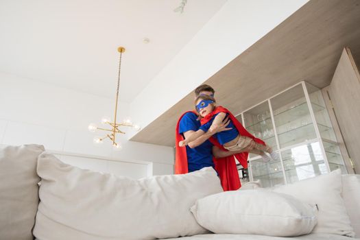 Father holding son flying in superhero costume at home