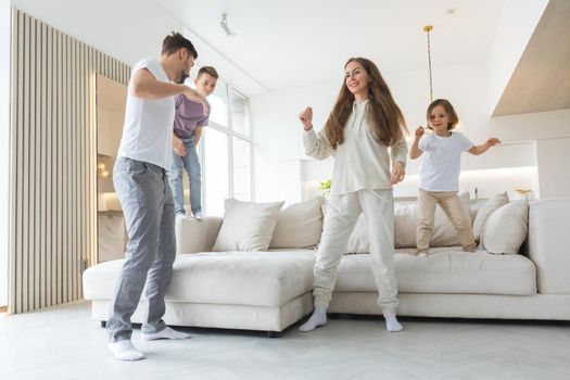 Family having fun at home. Married couple with little kids dancing moving in living room. Happy family spend time together concept